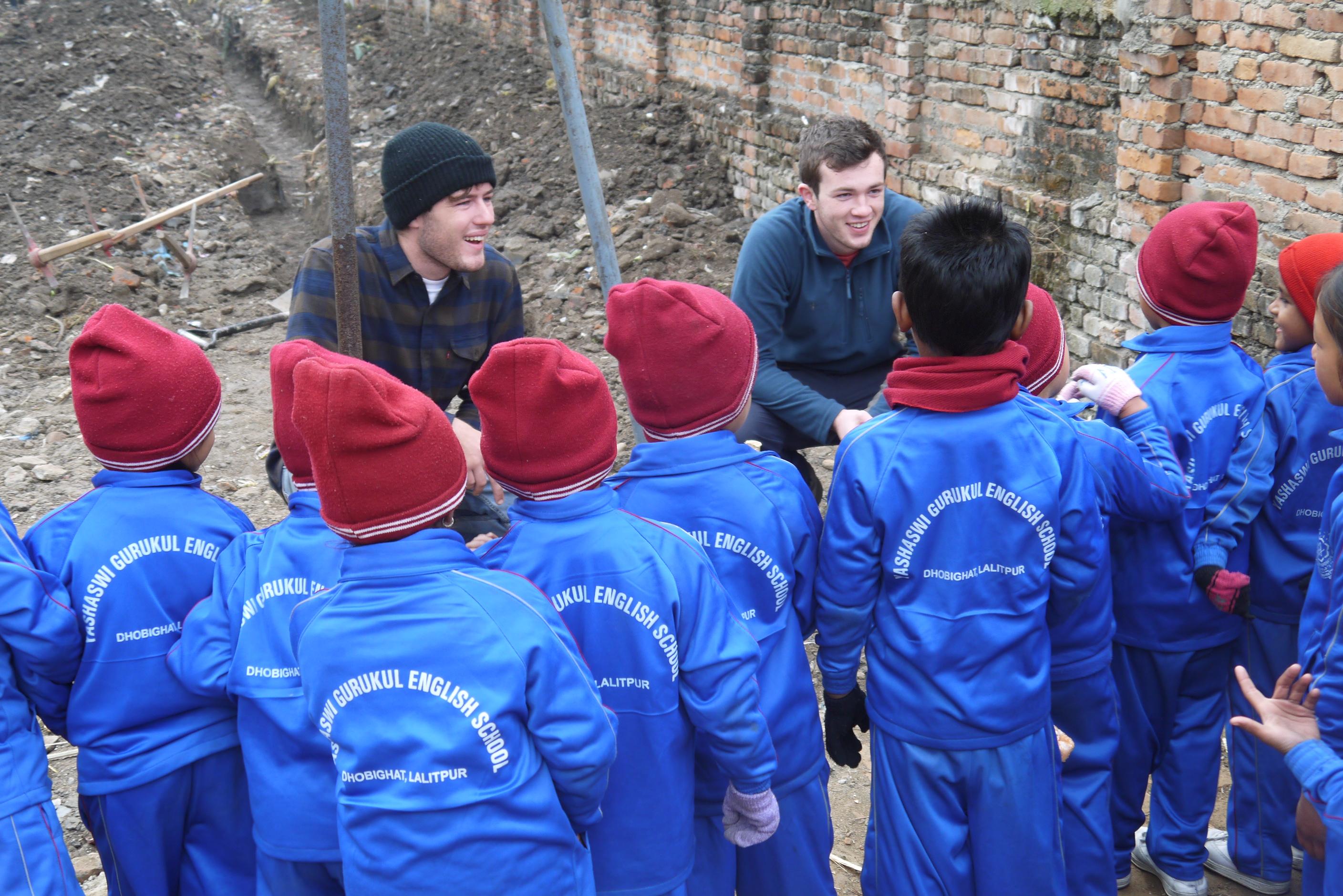Projects Abroad high school student volunteers doing construction work in Nepal take a break to talk to young children. High school student volunteers doing building work in Nepal stop working to talk with young children.
